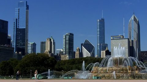 Buckingham Fountain in Chicago on a summer day. A plane flies through the scene in the background as tourists mill around and pose for photos