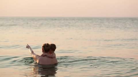 Loving mother and her young child bathing in the sea water by the beach in the sunset Stockvideo