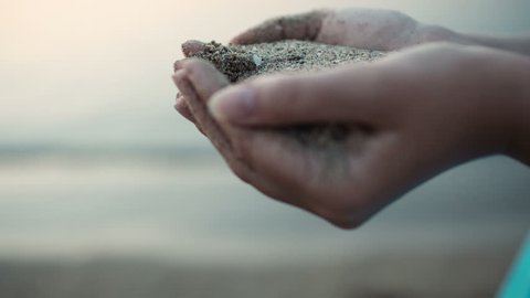 Close up view of sea sand running through a womans hands against a blurred ocean backdrop with copyspace conceptual of a summer vacation