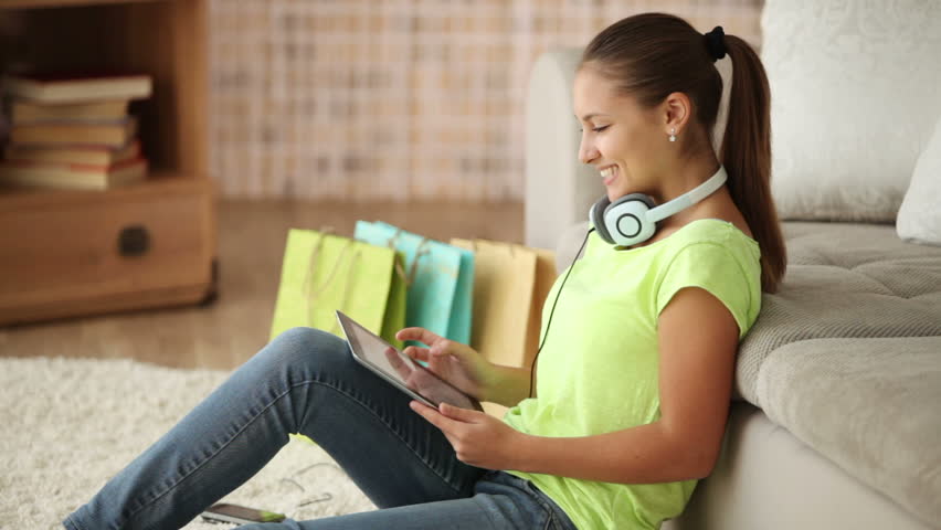 Beautiful girl in headphones sitting on floor using touchpad and smiling at