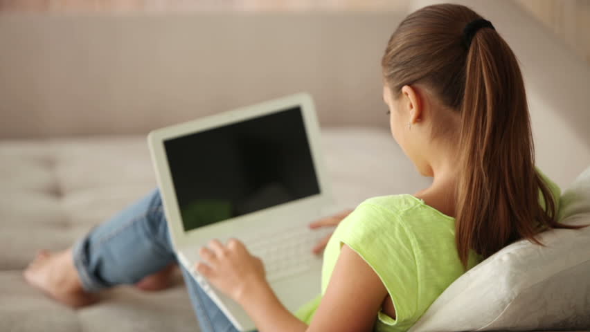 Attractive girl sitting on sofa using laptop looking at camera and smiling