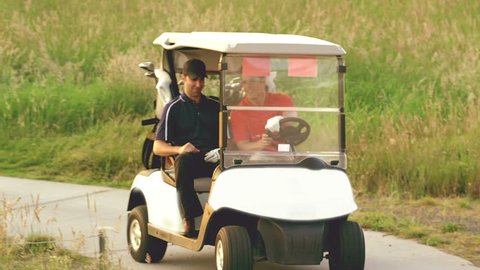 Two men drive a golf cart around a golf course and then stop to play their ball