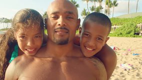A man and his two children sit at the beach and smile into the camera