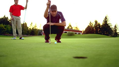 A man lines up a putt as his friend watches and takes the shot