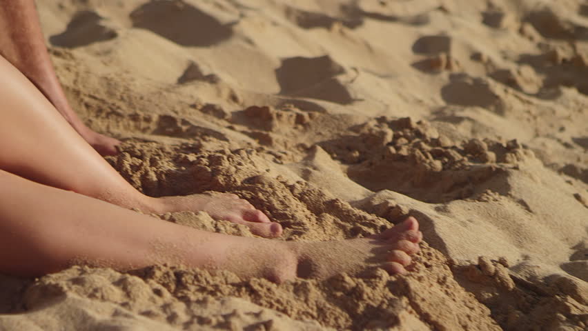 An older couple sit in the sand at the beach and look through a tablet