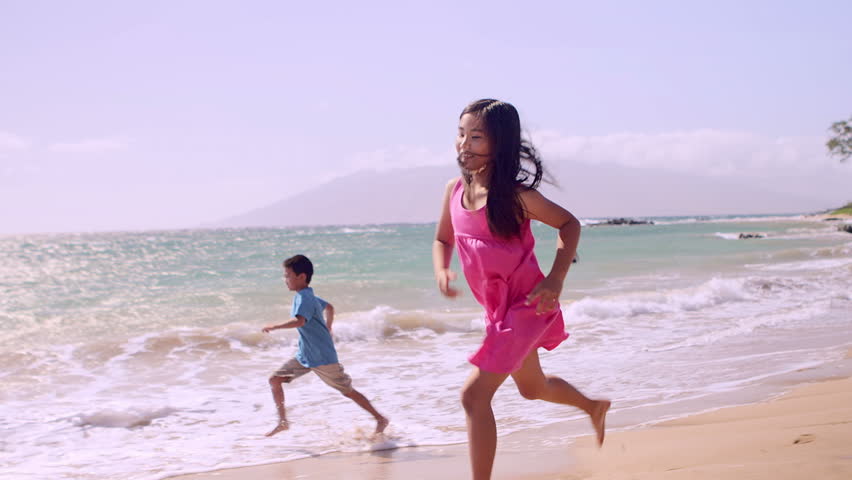 A young boy and girl run down the beach in slow motion next to the ocean