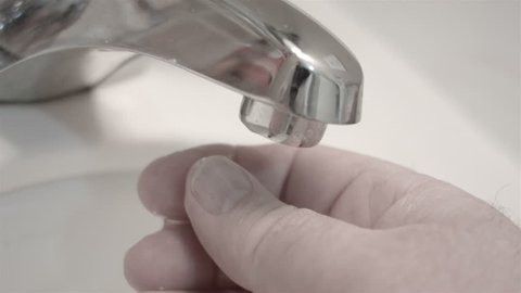 Man hand under dripping bathroom tap HD. Fresh clean flowing water from chrome silver bathroom sink tap. Wasting water by leak. White marble background. 