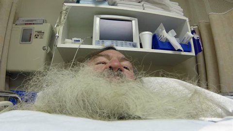 Man with big beard recovery hospital bed HD. Breathing motion. Mature man laying in recovery bed at ER emergency same day surgery hospital. Post medical procedure waking up after anesthesia. 