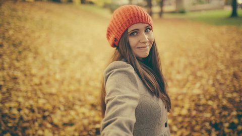 Young woman pulling her boyfriend through autumn park with leafs pov