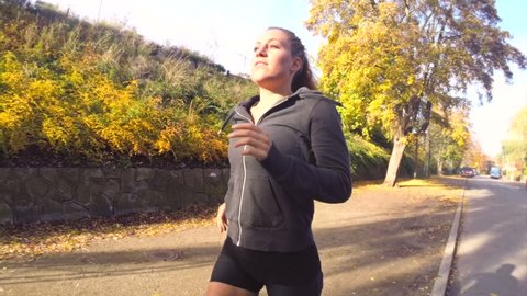 Sunny Autumn Run. Young active female athlete exercising outdoor in the sunny autumn. Running close to a park. Healthy women.