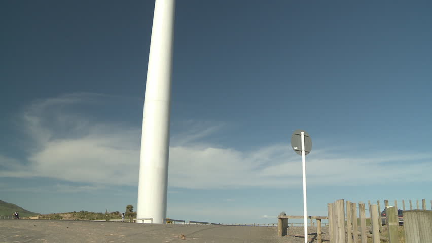 A tilt up shot from the base of a wind turbine tower to the blades and generator