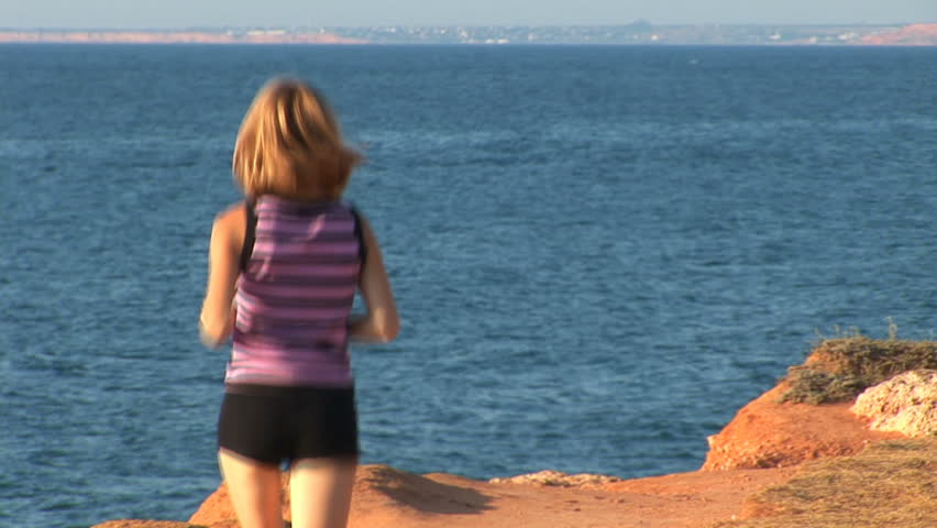 Girl plays sports on seacoast. She runs. Escapes from a videocamera