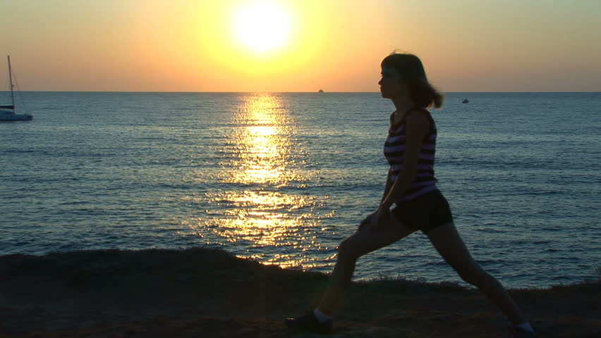 Girl does stretches against the sea during sunset. The yacht sails by in the