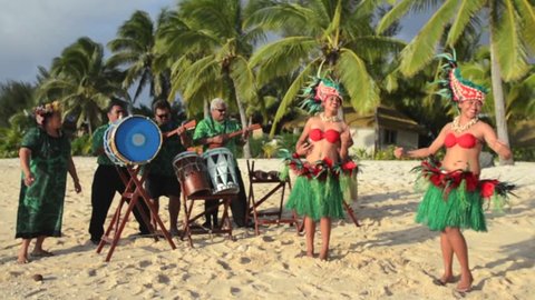 Polynesian Pacific Island dance and music group in colorful costumes dancing on tropical beach with palm trees in the background in Rarotonga Cook Islands. Real people. Copy space