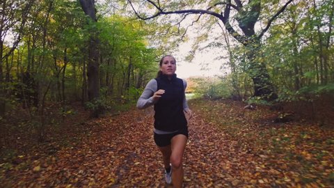 Active woman trail running in forest in the fall / autumn season. Exercising for a healthy body. Model is caucasian in the 20s.

