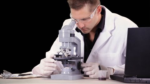 A young man who appears to be a scientist or lab technician working with a microscope and laptop. Close up with luma matte