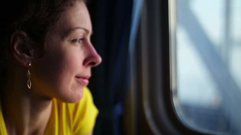 Flashes of sunlight on women face which watches in window of train during ride by bridge