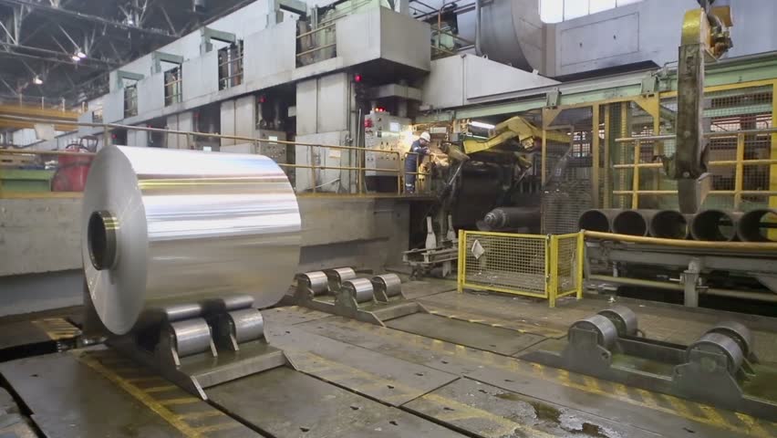 Man works in workshop with transporter which moves big roll of aluminum at metallurgical plant