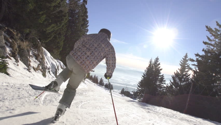 Slow Motion Rear View Of Skier Carving Down Steep Slope On A Sunny Winter Day.