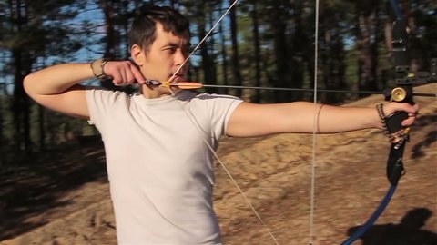 The young man is shooting from the sports bow in a sunny forest. 
This clip was shot in a slow motion (59 fps, 1280x720).