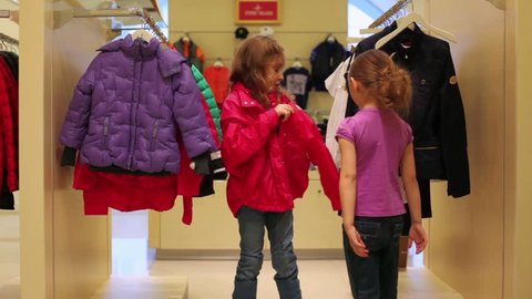 Girl helps to dress in red jacket in the clothing store