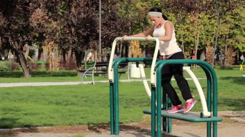 The girl exercising on gym equipment in the park,wide angle shot, sunny day.