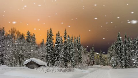Falling snow on a quaint log cabin nestling in a snow covered evergreen forest under a beautiful glowing orange sunset sky