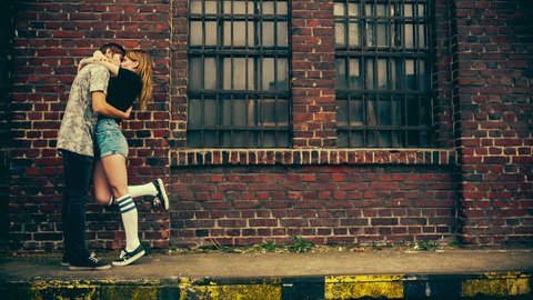Teenage couple kissing in front of old industry building with vintage color correction Stock Video