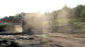 Big truck is in motion and is leaving the site barricaded by a stop sign to get another batch of gravel. A dump truck is done unloading the sand and gravel on a construction area