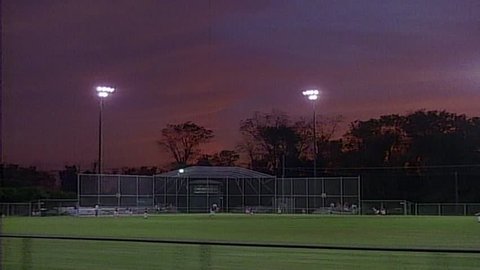Highschool baseball game at dusk tracking shot from right to left