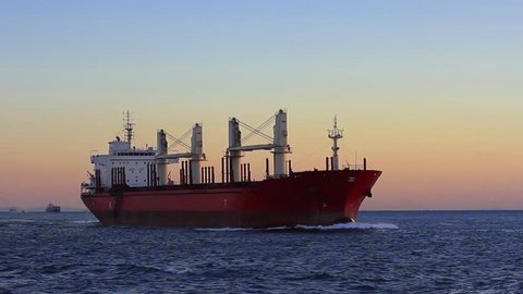 Cargo ship sailing from open sea. A bulk carrier ship with deck cranes on the sunset time.
