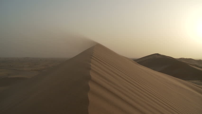 Strong winds blow desert sand over a sand hill 