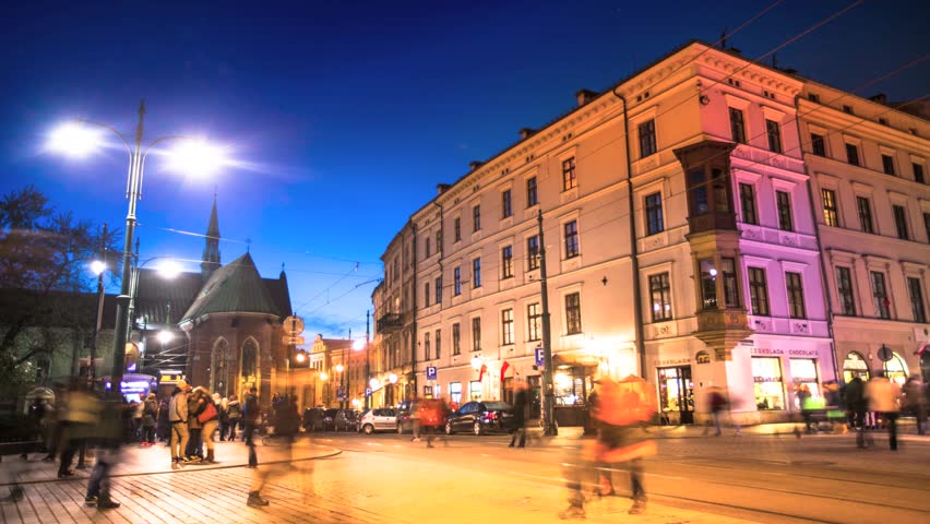 On the busy street in the center of Krakow at night time, near the main square,