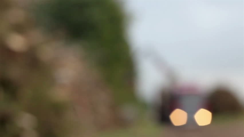 Vehicle moving on a highway where trees are found at the side and a big open field found at its back. A long and empty highway;with few cars passing by with the weather is foggy and trees on roadside.