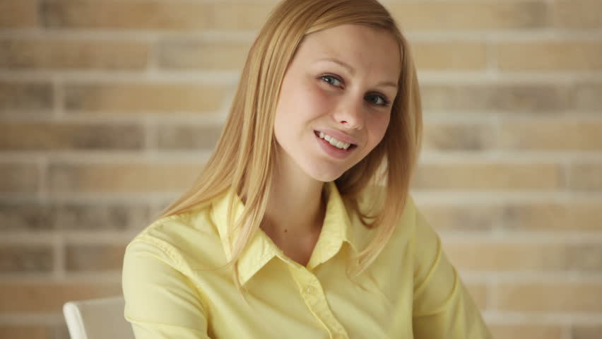 Pretty young woman sitting at table using laptop looking at camera and smiling.