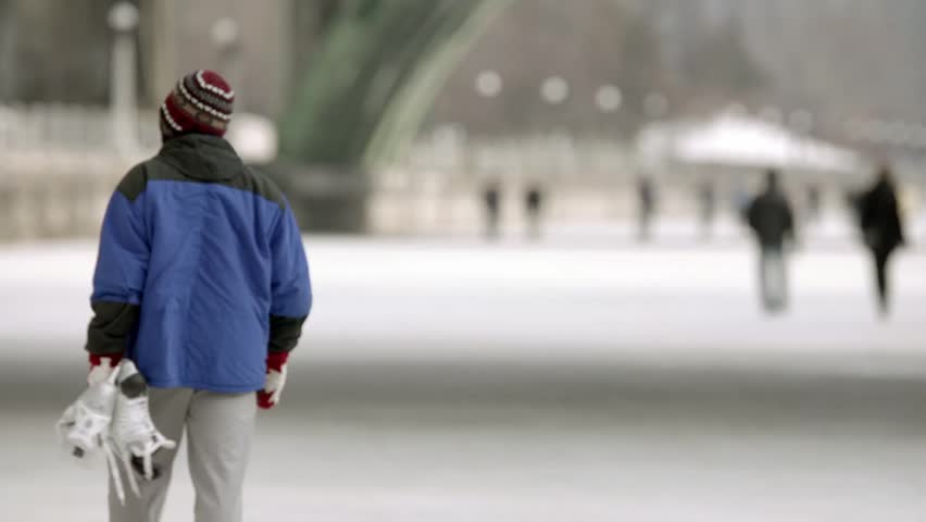 Man walking on the Rideau Canal holding his skates.