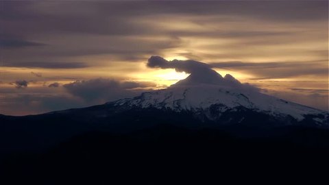 Mt Hood at Sunrise - CLOSE. The clouds swirl above Mt. Hood as the sunrises behind. Beautiful golden sky