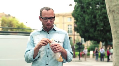 Man eating baguette standing by the city street
