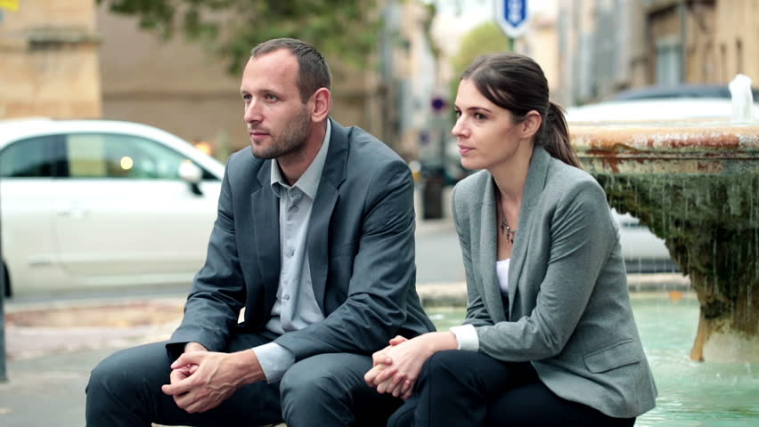Confident young business people sitting on fountain in the city
