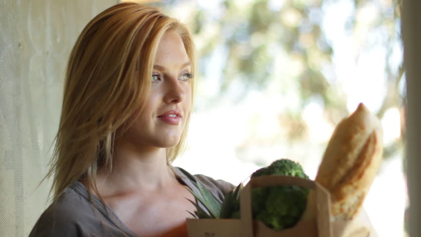 Attractive young blonde woman waits and then delivers groceries to a home.  No