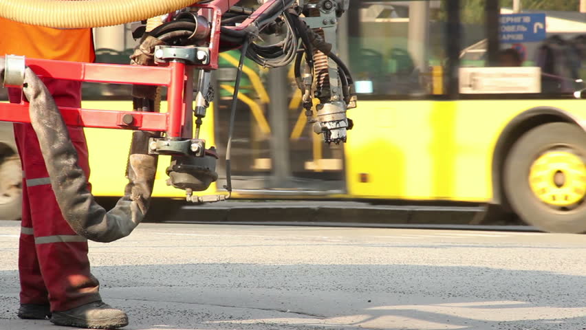 Worker fixing road with patching machine, city daytime traffic