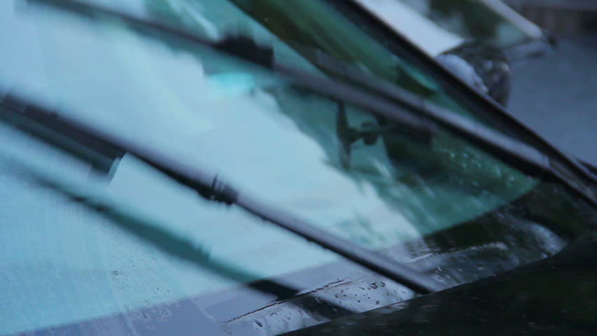 Windscreen wipers on car front glass tearing rain drops, daytime