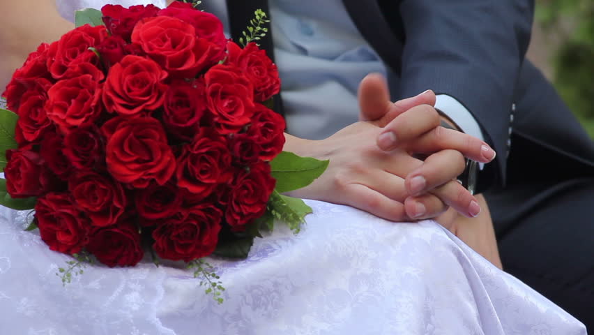 Newlyweds bride and groom on bench with bouquet of roses