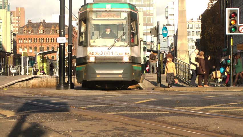 MANCHESTER CIRCA 2013: Tram drives away from a stop with pedestrians in the
