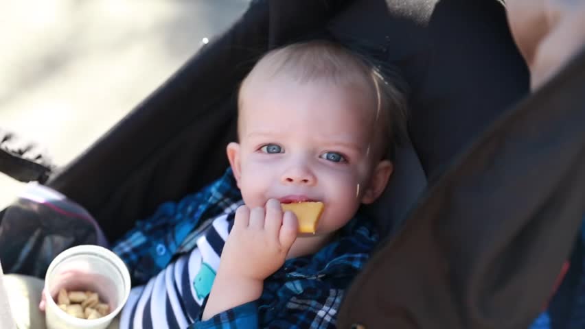 A baby boy eating his lunch in the stroller