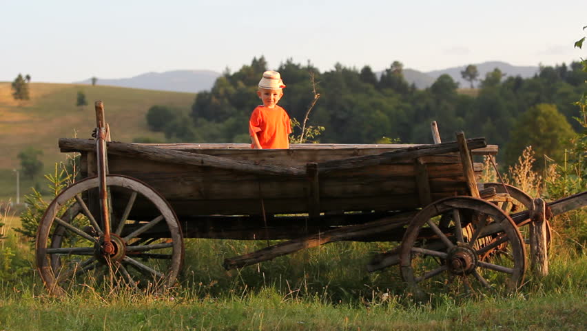 Lovely peasant child with a traditional cap, sit in traditional wooden cart