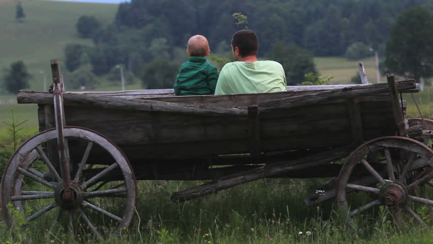 Baby son and young father admire green nature, sit in traditional wooden cart