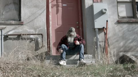 Homeless man sitting on steps sad and poor 2 HD. Red plaid shirt and red cup for drink and drinking. Evicted and now his dynasty is over. Homeless man down on luck, poor, hungry and depressed.