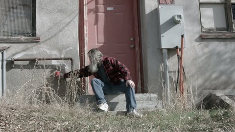 Homeless man broken poor long hair beard 2 HD. Drinking from red cup from dripping tap. Warm plaid shirt for warmth. Down on luck, poor, hungry and depressed sits on steps of abandoned building.