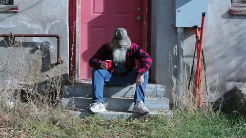 Homeless man camo hat sad poor hungry HD. Red plaid warm shirt and camouflage baseball hat. Homeless man down on luck, poor, hungry and depressed sits on steps of abandoned building.